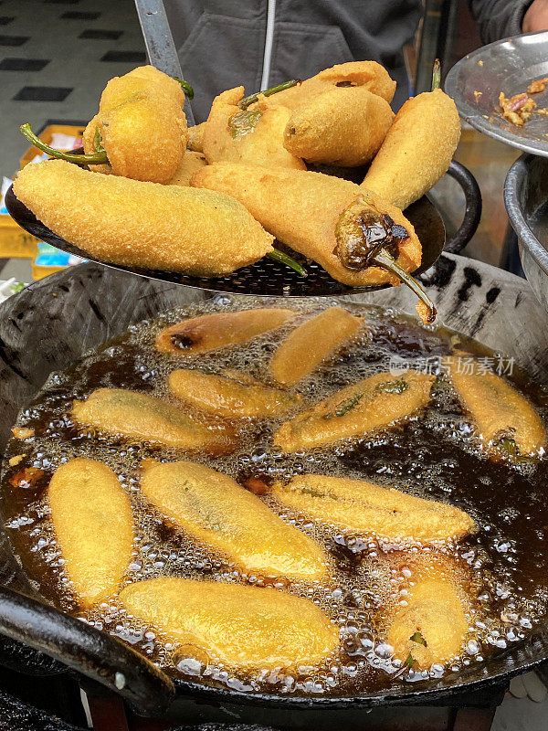 一个不认识的人在煮绿辣椒油饼(mirch pakora)，在大油锅里油炸，印度街头小吃摊贩，印度街头小吃摊档，不健康的饮食，高架视野，重点在前景